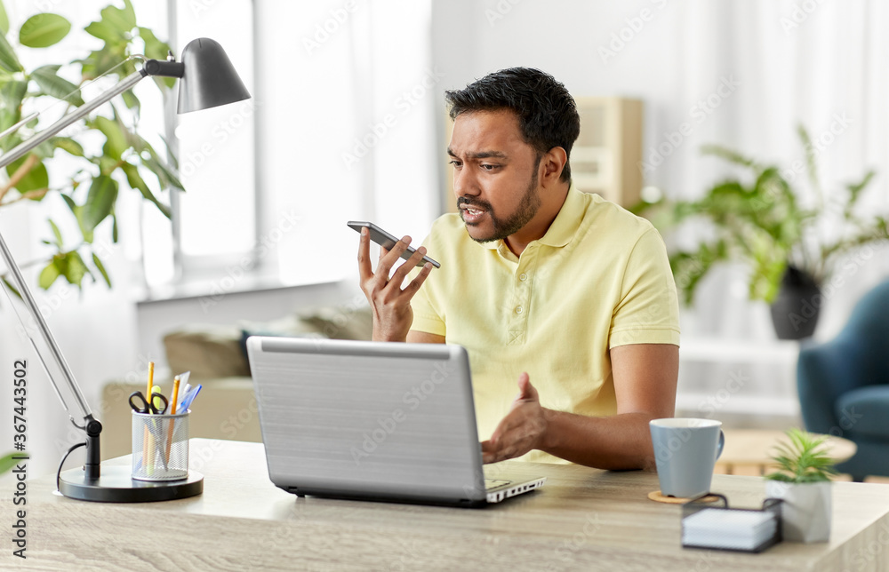 technology, communication and people concept - angry indian with smartphone and laptop computer using voice command recorder at home office