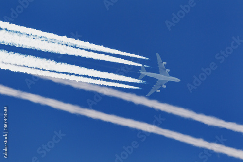 Large four engined commercial airliner jet aircraft flying at high altitude with a large contrail flowing behind it.