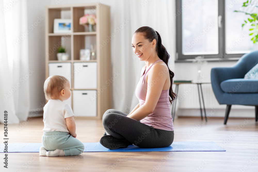 family, sport and motherhood concept - happy smiling mother with little baby sitting on exercise mat at home