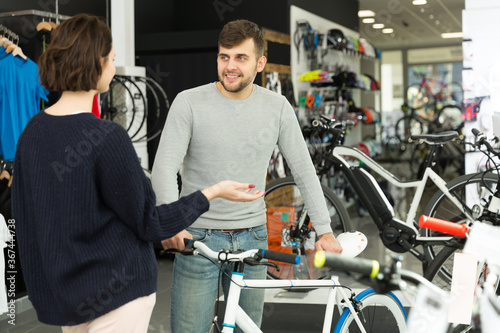 ..Portrait of young man seller showing bicycle to woman in bicycle shop