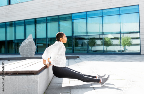 fitness, sport and healthy lifestyle concept - young african american woman doing bench triceps dip outdoors