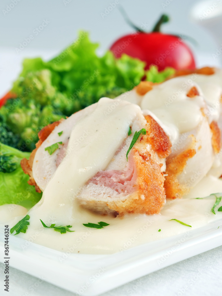 Chicken cordon bleu sliced with parmesan cream sauce and vegetables, vertical Chicken cordon bleu sliced with parmesan cream sauce and vegetables, vertical