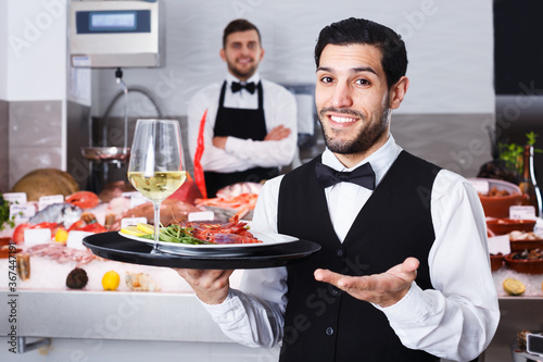 Smiling bearded waiter standing with serving tray in seafood restaurant