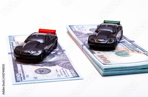 Two sports cars in black on two piles, piles of dollar bills podium. One pile, a pile more, another less. The difference in the price of the car. Buy, sell, rise and fall of prices in the market