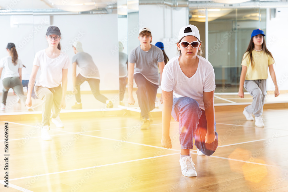 Group of teenagers in casual clothes training hip-hop in class, learning modern dance movements