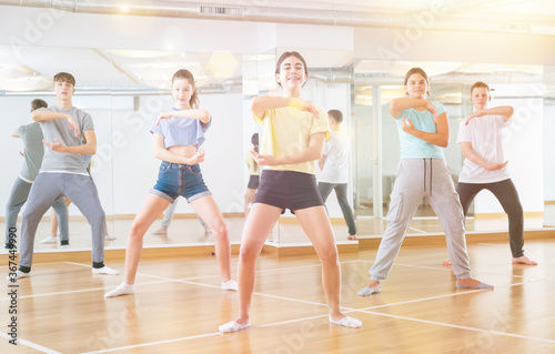 Diligent friendly smiling teenagers learn dance movements in dance class