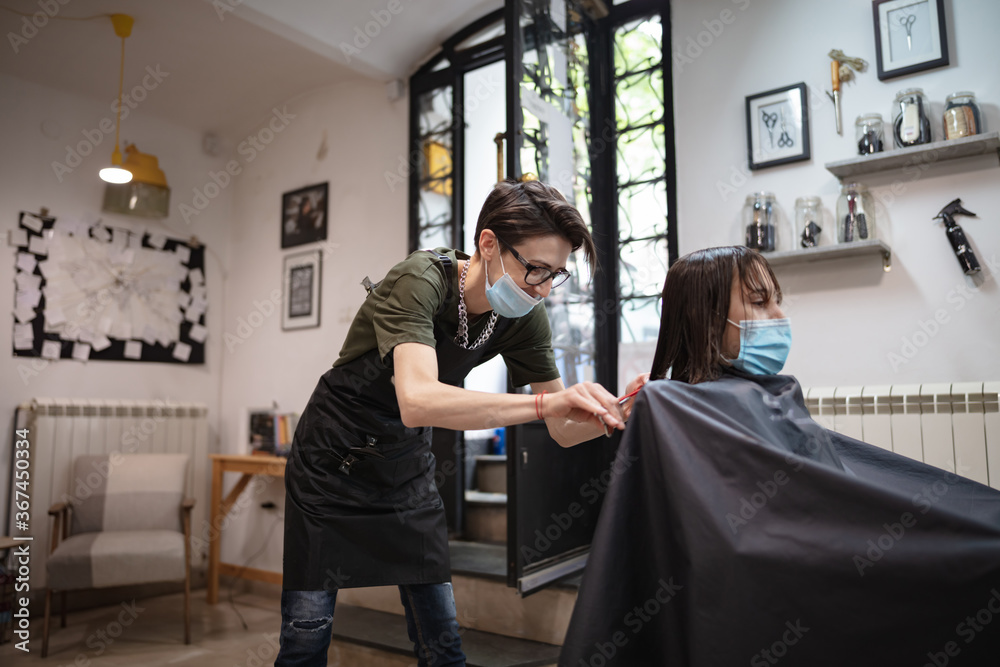 Hairdresser and girl child customer in a salon with medical masks during virus pandemic. Working with safety mask. Hairdresser and girl child customer in a salon with medical masks during virus pandemic. Working with safety mask.