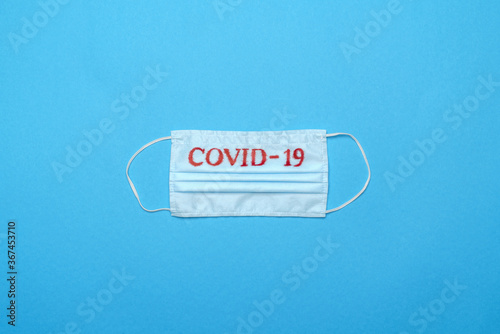 Disposable blue medical face mask with COVID-19 sign on blue background