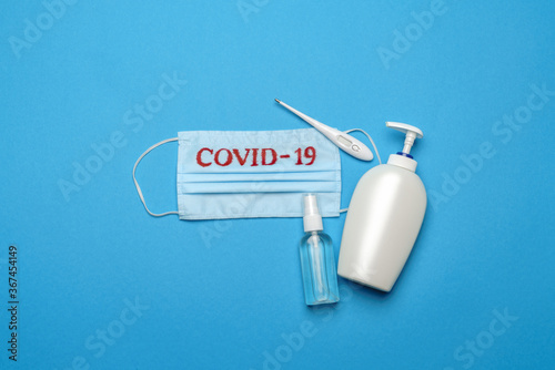 Disposable blue medical face mask with COVID-19 sign, electrinic thermometer and alcohol hand sanitizer antiseptic on blue background photo