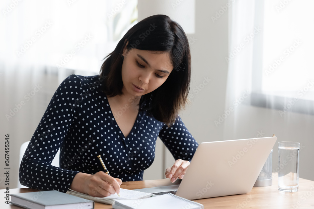 Concentrated Asian millennial girl sit at desk study make notes using modern laptop, focused Vietnamese young woman handwrite take online course or distant training on internet on computer from home Concentrated Asian millennial girl sit at desk study make notes using modern laptop, focused Vietnamese young woman handwrite take online course or distant training on internet on computer from home