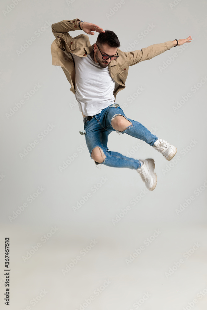 cool young man in jacket looking down and jumping