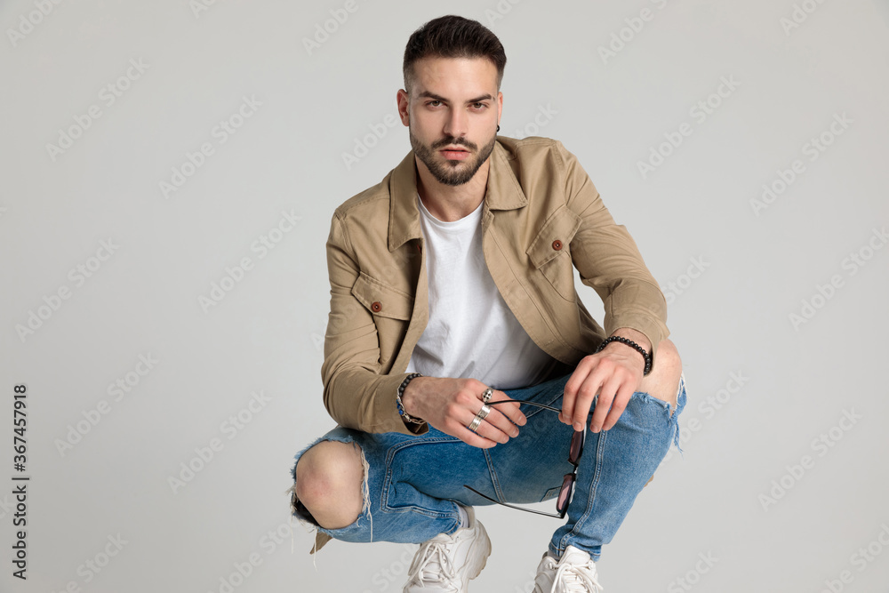 handsome young casual man in jacket holding elbows on knees handsome young casual man in jacket holding elbows on knees