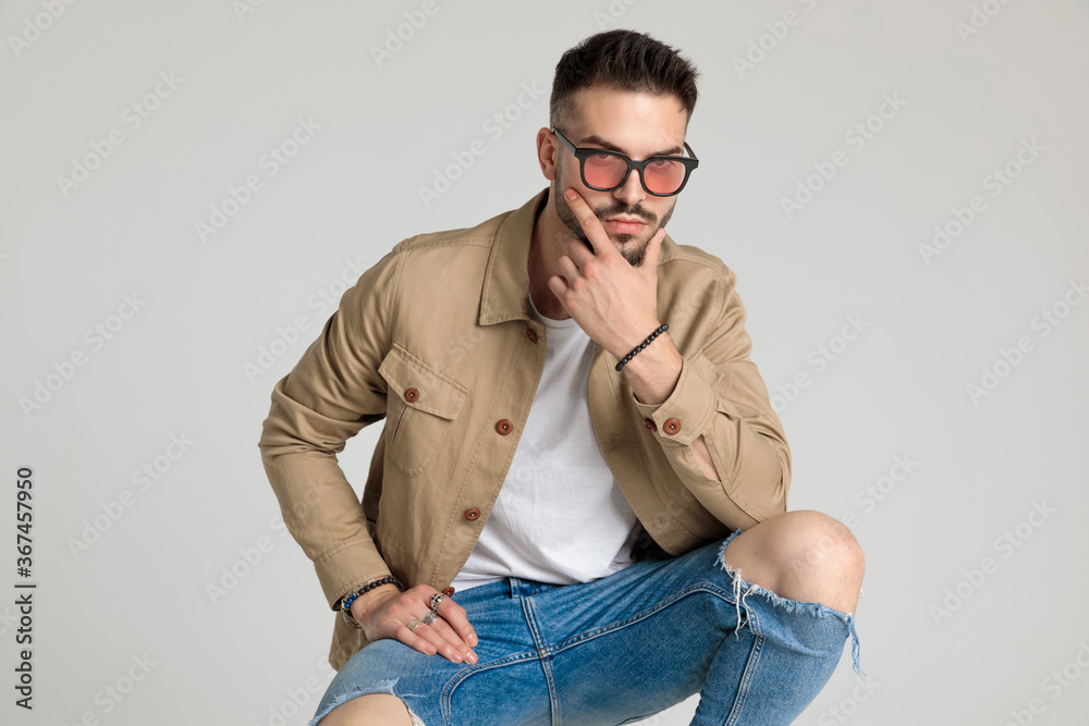 young casual man in beige jacket holding hand to chin and thinking young casual man in beige jacket holding hand to chin and thinking