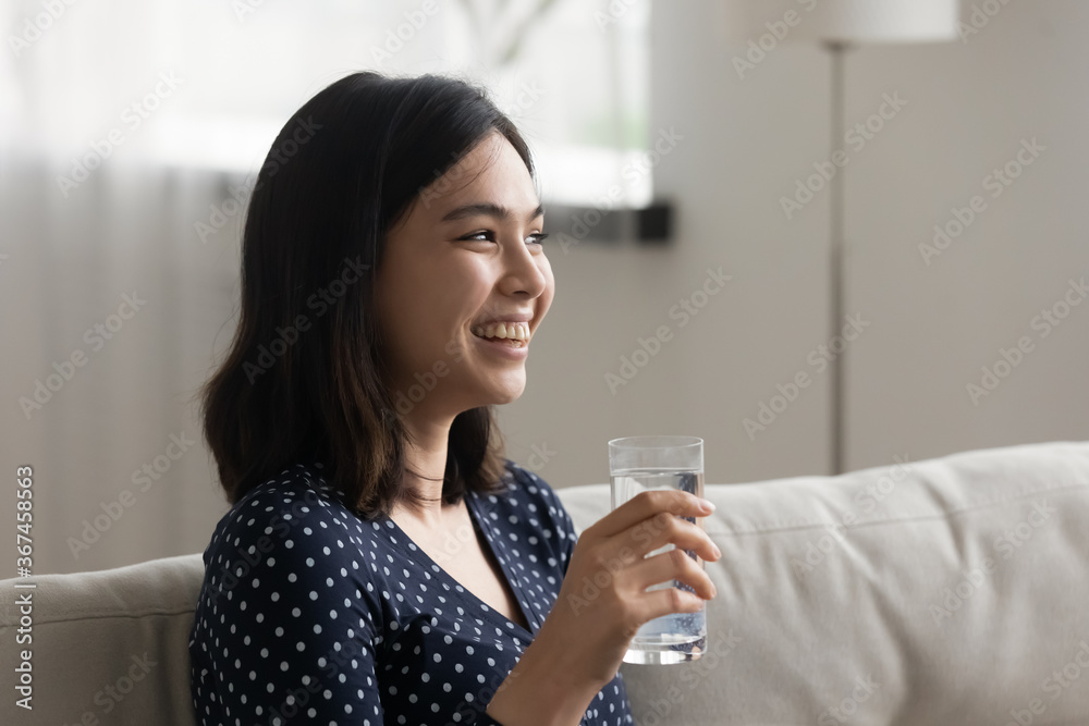 Smiling millennial Vietnamese girl relax on sofa at home drink clean clear mineral water from glass, dehydrated thirsty Asian woman enjoy crystal pure aqua, hydration, healthy lifestyle concept Smiling millennial Vietnamese girl relax on sofa at home drink clean clear mineral water from glass, dehydrated thirsty Asian woman enjoy crystal pure aqua, hydration, healthy lifestyle concept