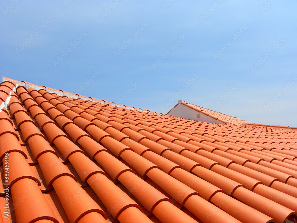 Red tile roof under blue sky. The photo is divided in half. One part is a roof made of clay tiles and the other is a pure blue sky. - obrazy, fototapety, plakaty 