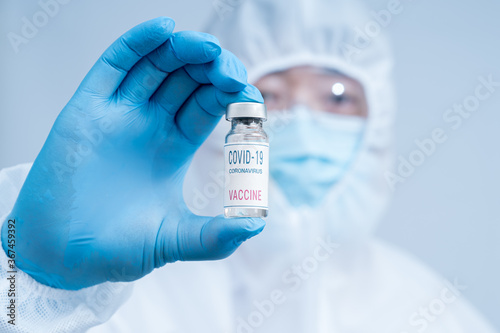 A male scientist wearing blue gloves and a protective suit holding a Covid-19 vaccine.