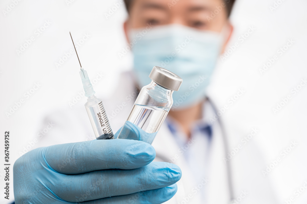 The doctor's hand wearing blue gloves against white background and holding Covid-19 vaccine.