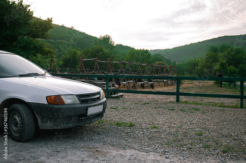 White station wagon in the mud is parked in the countryside. White car in the mud stands on a background of green trees. © Ilya_R