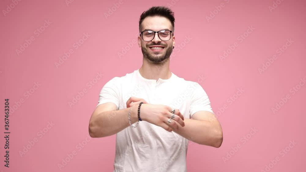 young handsome casual man standing with his arms folded, wearing eyeglasses, looking down then raising his head, smiling, giving a thumbs up with both dancing hands on pink background young handsome casual man standing with his arms folded, wearing eyeglasses, looking down then raising his head, smiling, giving a thumbs up with both dancing hands on pink background