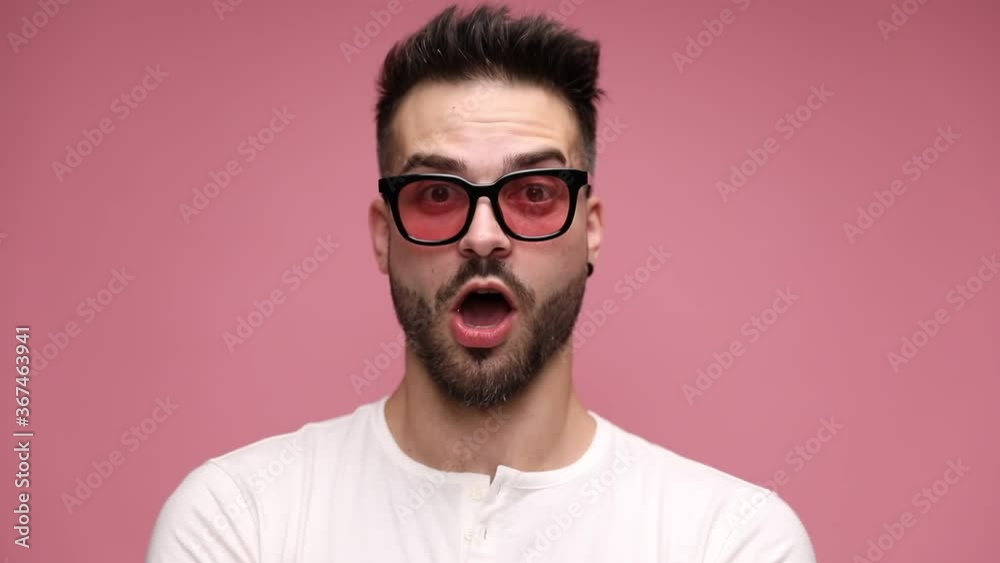 close up of a casual man looking at camera, being serious then adopting a fearful expression on his face, being surprised then happily surprised on pink background