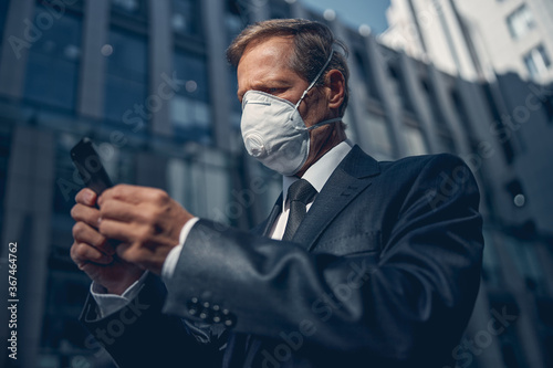 Handsome man in medical face mask using cellphone outdoors