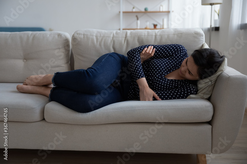 Sad young Vietnamese woman lying on sofa at home suffer after miscarriage or abortion, unhappy millennial Asian girl feel distressed upset struggle with depression or mental psychological problems