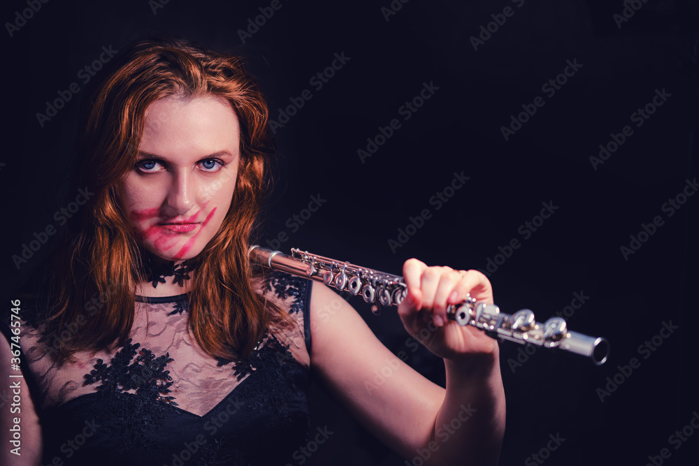 Woman vamp with a flute on his shoulder, concept musician for halloween. Redhead woman with lipstick smeared on her face, copy space on black background