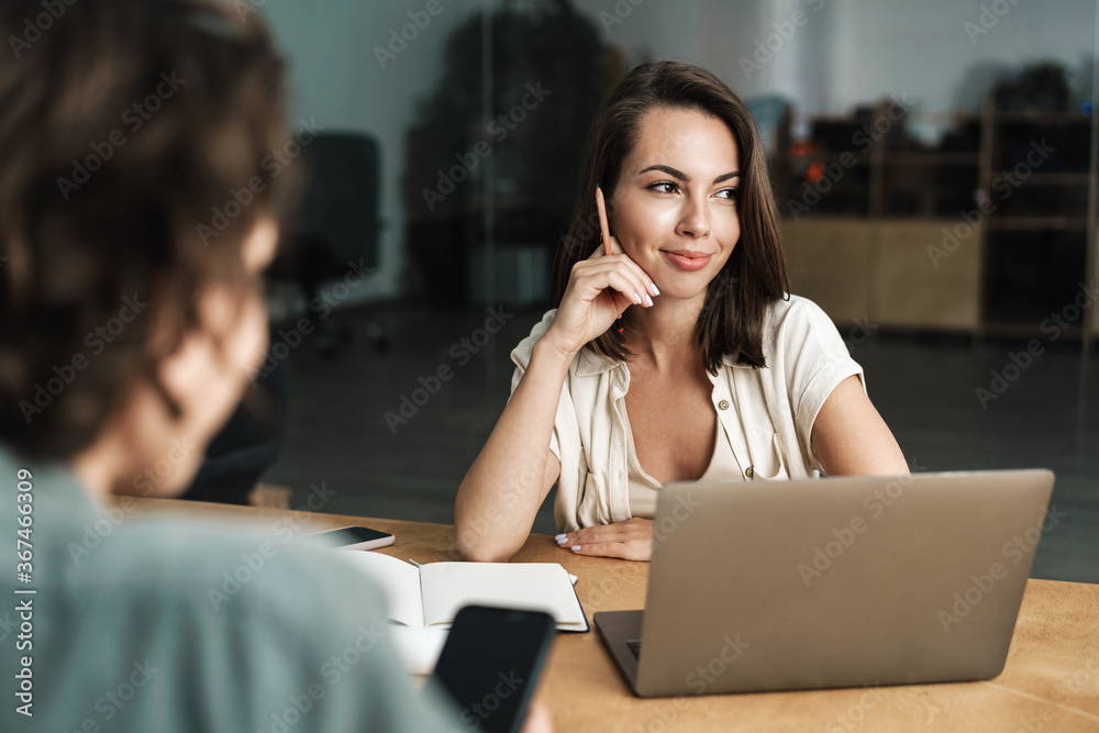Image of young smiling colleagues working with laptop and mobile phone Image of young smiling colleagues working with laptop and mobile phone