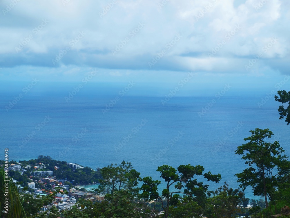 Beautiful seascape, view from the top to the bottom. Cloudy sky, blue water, threes on the foreground. Tropical island. Open sea and rainforest, amazing heaven. Panorama of ocean. Coastal town. 