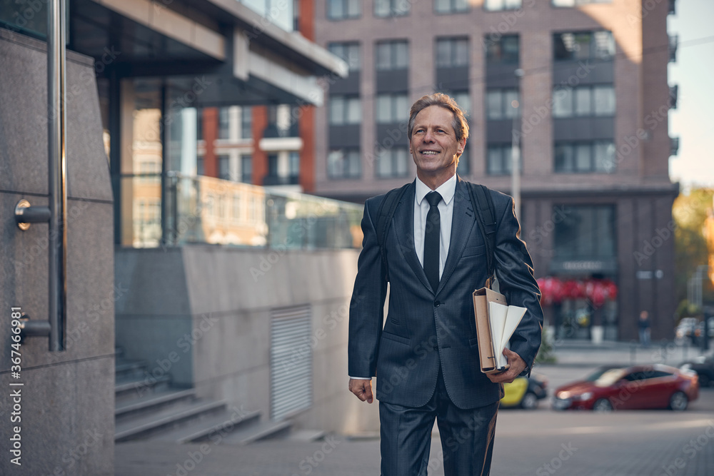Cheerful businessman with papers walking on the street Cheerful businessman with papers walking on the street