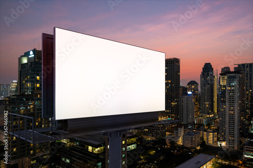 Blank white road billboard with Bangkok cityscape background at night time. Street advertising poster  mock up  3D rendering. Side view. The concept of marketing communication to sell idea.