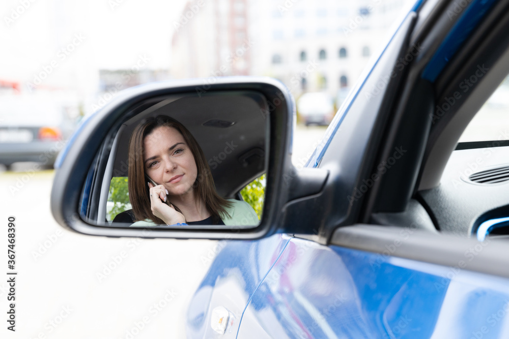 A girl in business clothes looks in the side view mirror and talks on the phone