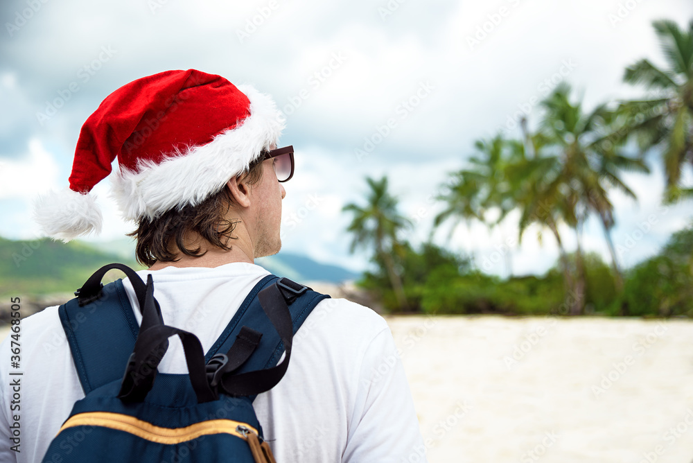 Obraz premium Happy man in red hat of Santa Claus and sunglasses at tropical beach. New Year or Christmas vacation concept