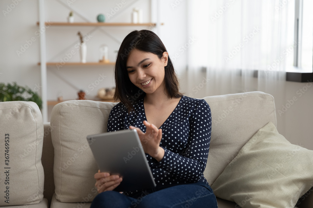 Smiling Asian millennial girl sit relax on couch in living room browse internet on modern tablet gadget, happy Vietnamese young woman rest on sofa at home using pad device, technology concept Smiling Asian millennial girl sit relax on couch in living room browse internet on modern tablet gadget, happy Vietnamese young woman rest on sofa at home using pad device, technology concept