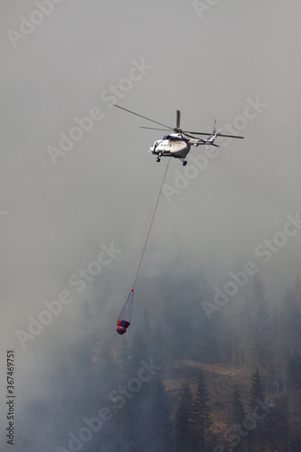 Forest fire. Firefighting helicopter lowers water under fire of helicopter and extinguishes huge forest fires. Special helicopter in flight suspension with a fire extinguishing drainage device