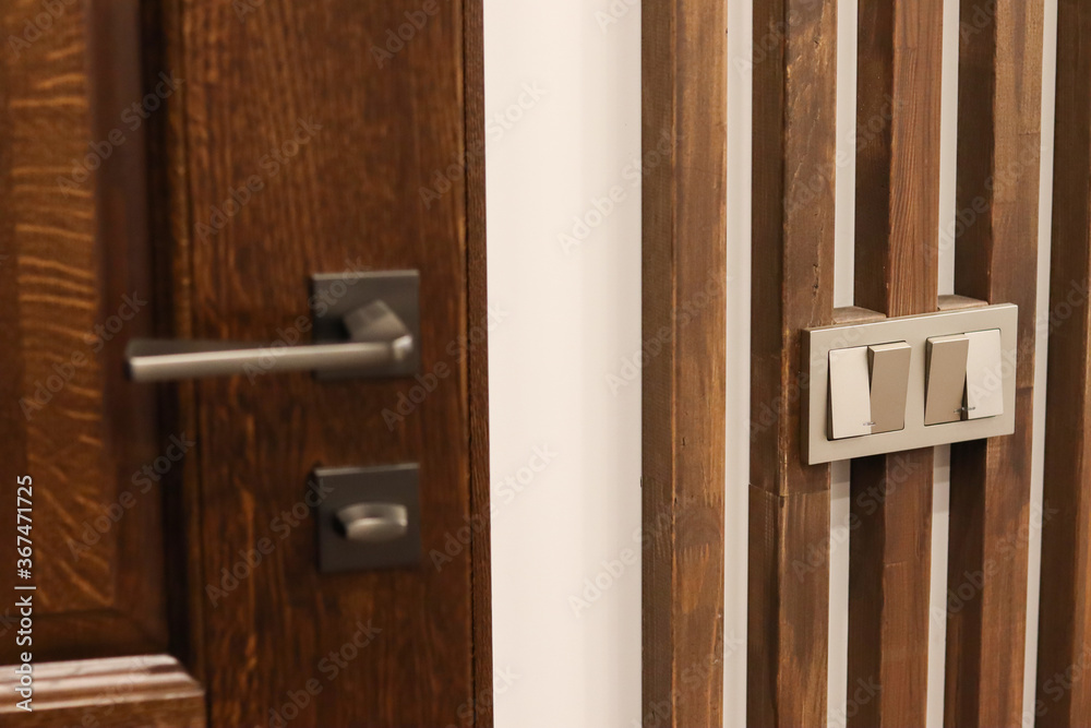 Fototapeta premium Wooden oak interior door, modern doorknob and switches. Wooden decorative oak planks on the wall. Modern interior, solid wood, neoclassicism.