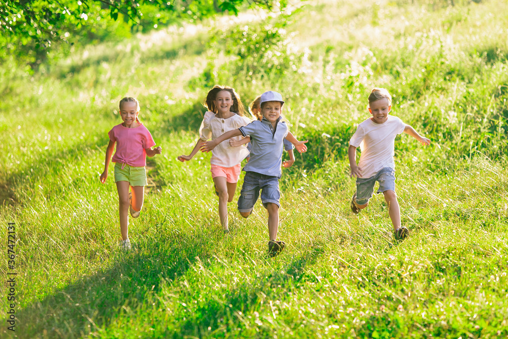 Obraz premium Kids, children running on meadow in summer's sunlight. Look happy, cheerful with sincere bright emotions. Cute caucasian boys and girls. Concept of childhood, happiness, movement, family and summer.