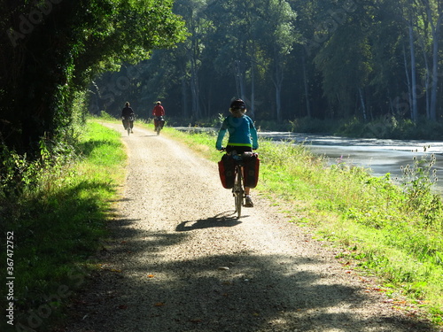 Jeune femme cycliste à vélo avec sacoche sur piste cyclable pour randonnée bicyclette le long d'un canal d'eau de rivière en France dans la Loire