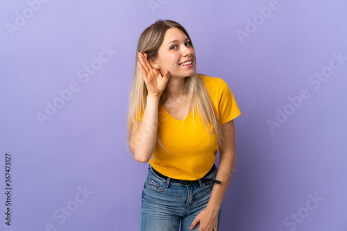 Young blonde woman isolated on purple background listening to something by putting hand on the ear © luismolinero