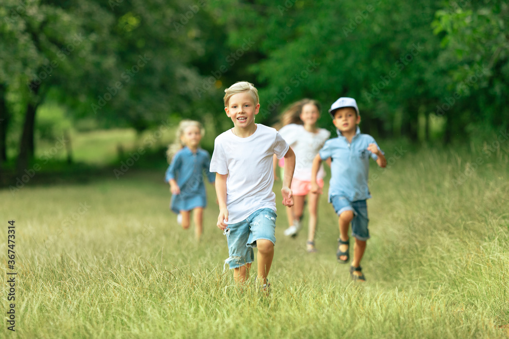 Kids, children running on meadow in summer's sunlight. Look happy, cheerful with sincere bright emotions. Cute caucasian boys and girls. Concept of childhood, happiness, movement, family and summer.