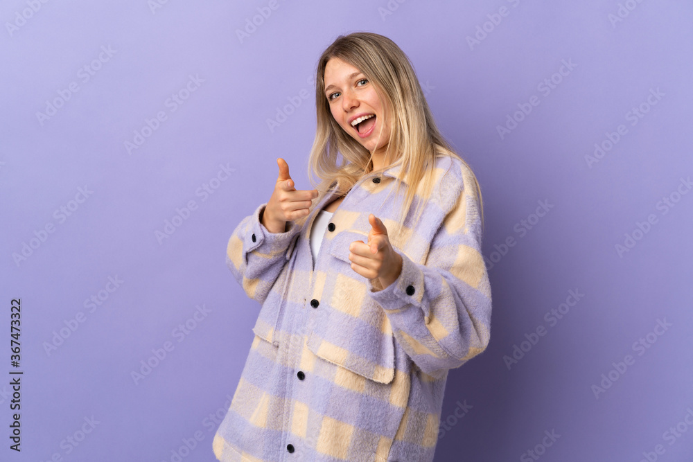 Young blonde woman isolated on purple background pointing to the front and smiling Young blonde woman isolated on purple background pointing to the front and smiling