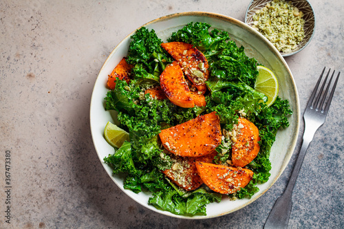 Baked sweet potato salad with kale in white bowl, dark background, top view. Vegan food concept. photo