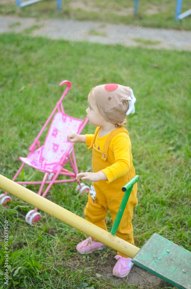 Photo of a toddler girl in the funny hat playing with a toy stroller