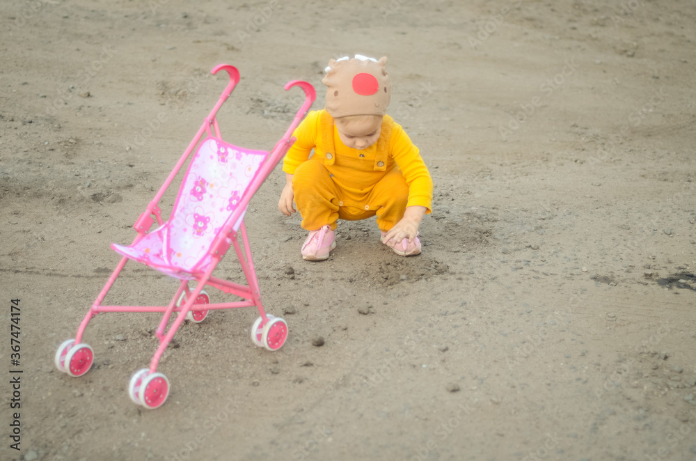 Photo of a toddler girl in the funny hat playing with a toy stroller Photo of a toddler girl in the funny hat playing with a toy stroller