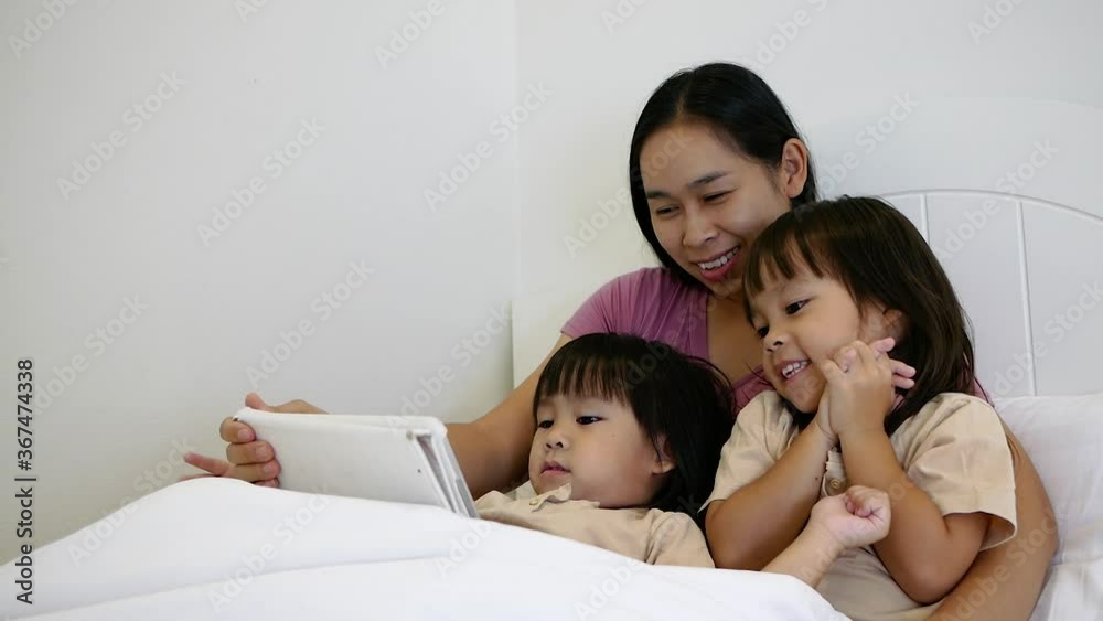 Happy mother and little daughters playing tablet pc computer on bed at night. Happy family time. Happy mother and little daughters playing tablet pc computer on bed at night. Happy family time.