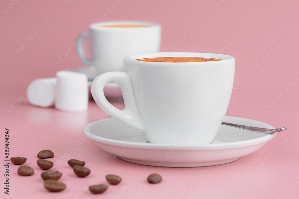 Two white cups of hot aroma coffee, some marshmallows and coffee beans on pink background. Morning coffee concept. Two white cups of hot aroma coffee, some marshmallows and coffee beans on pink background. Morning coffee concept.
