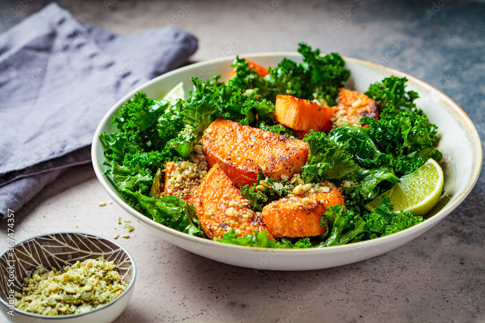 Baked sweet potato salad with kale in white bowl, dark background. Vegan food concept.