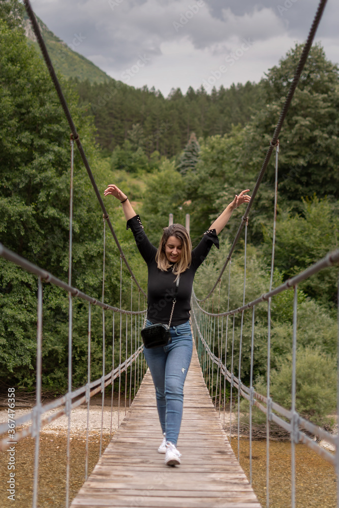 A young woman crossing a scary and narrow suspension bridge over a