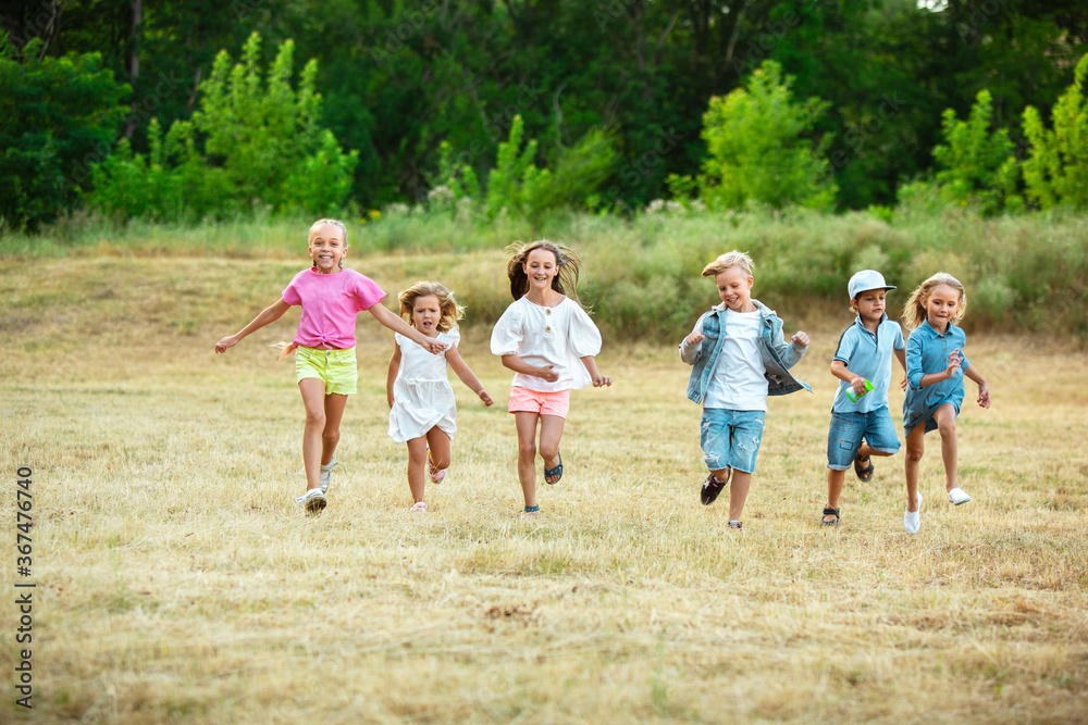Kids, children running on meadow in summer's sunlight. Look happy, cheerful with sincere bright emotions. Cute caucasian boys and girls. Concept of childhood, happiness, movement, family and summer. Kids, children running on meadow in summer's sunlight. Look happy, cheerful with sincere bright emotions. Cute caucasian boys and girls. Concept of childhood, happiness, movement, family and summer.