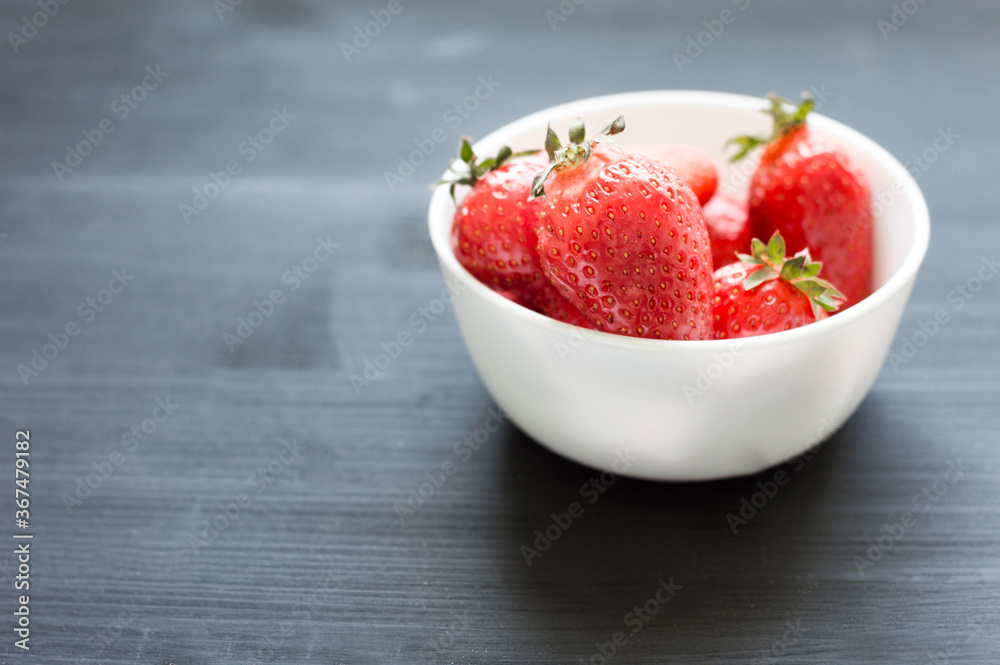 Fresh summer strawberry in the small white bowl on the black wooden backround Fresh summer strawberry in the small white bowl on the black wooden backround